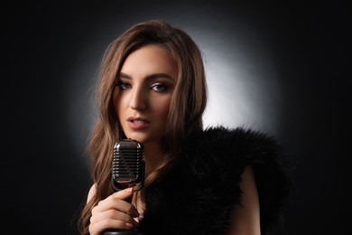 Beautiful young woman with microphone singing on black background