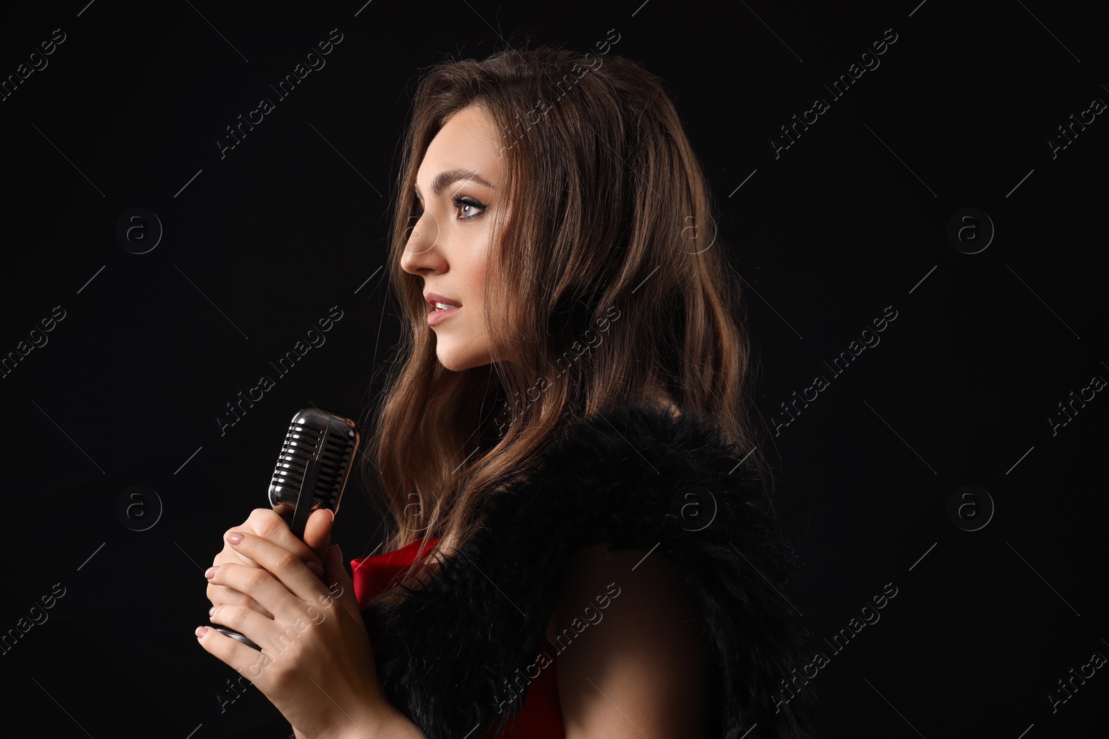 Photo of Beautiful young woman with microphone singing on black background