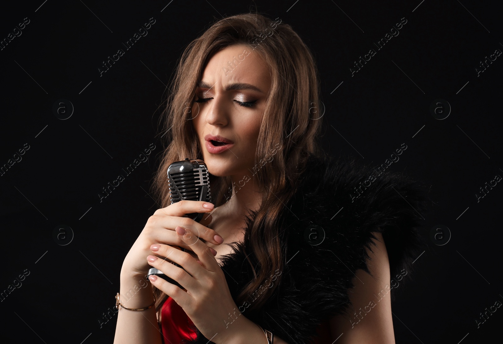 Photo of Beautiful young woman with microphone singing on black background