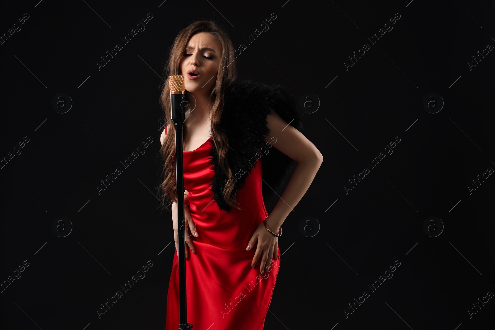 Photo of Beautiful young woman in stylish dress with microphone singing on black background