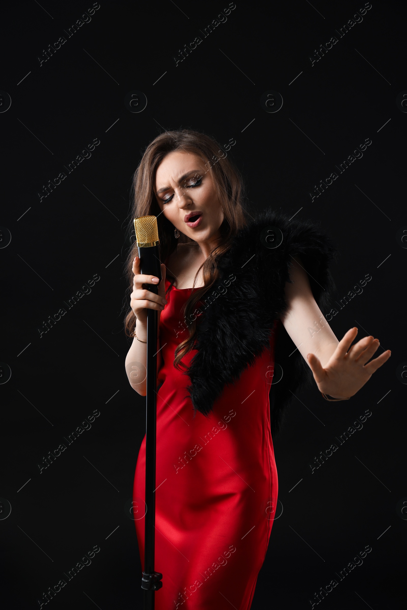 Photo of Beautiful young woman in stylish dress with microphone singing on black background