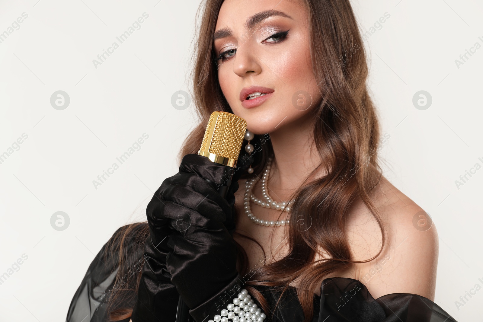 Photo of Beautiful young woman with microphone singing on light grey background