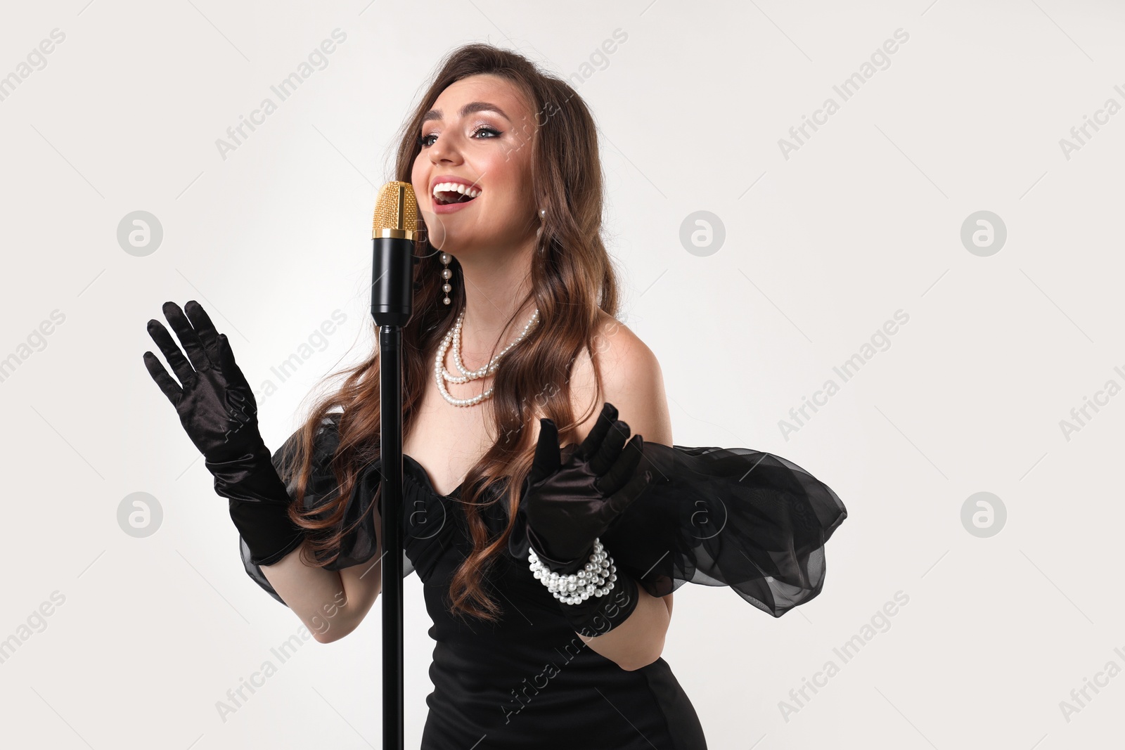 Photo of Beautiful young woman in stylish dress with microphone singing on light grey background