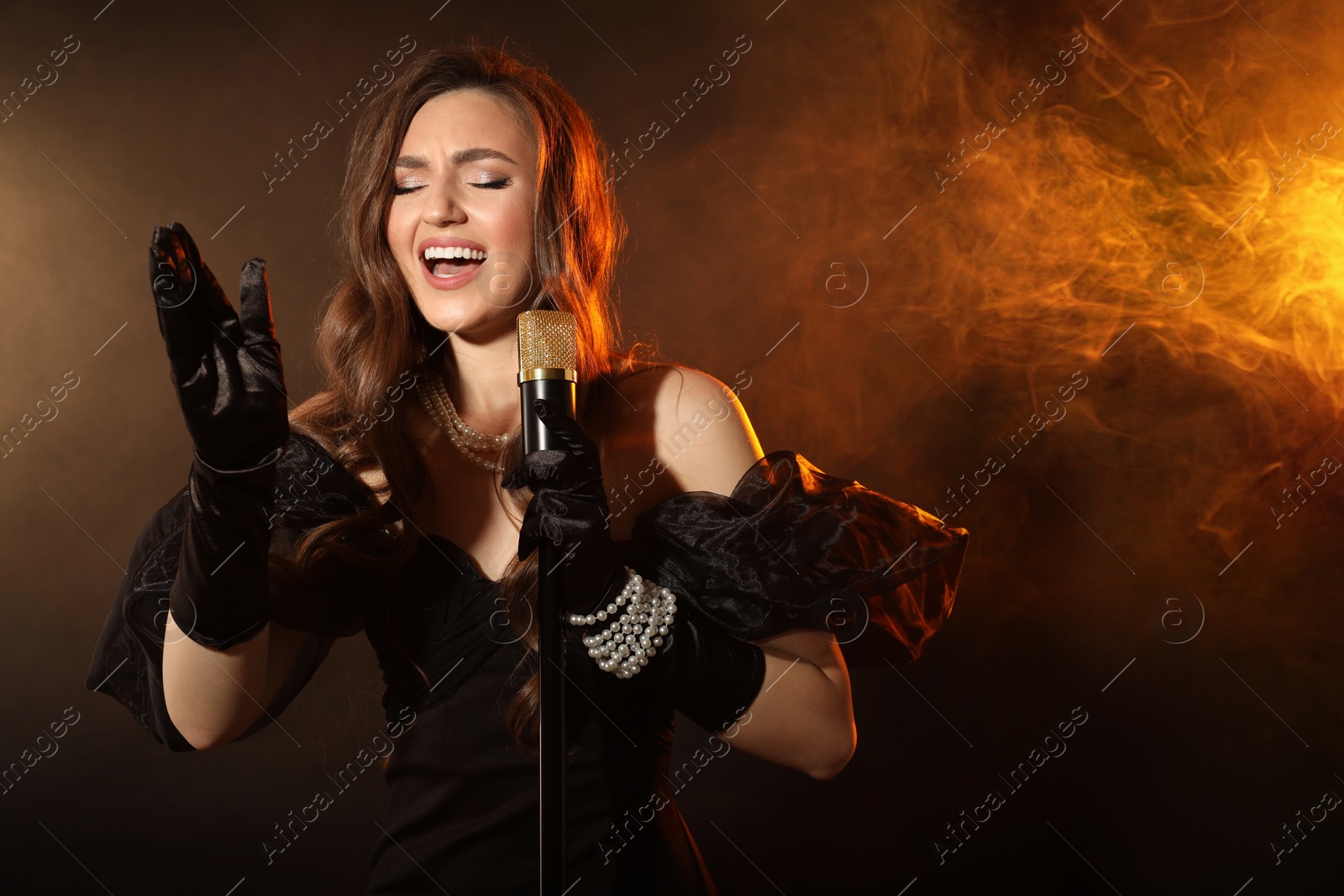 Photo of Beautiful young woman with microphone singing in color lights and smoke