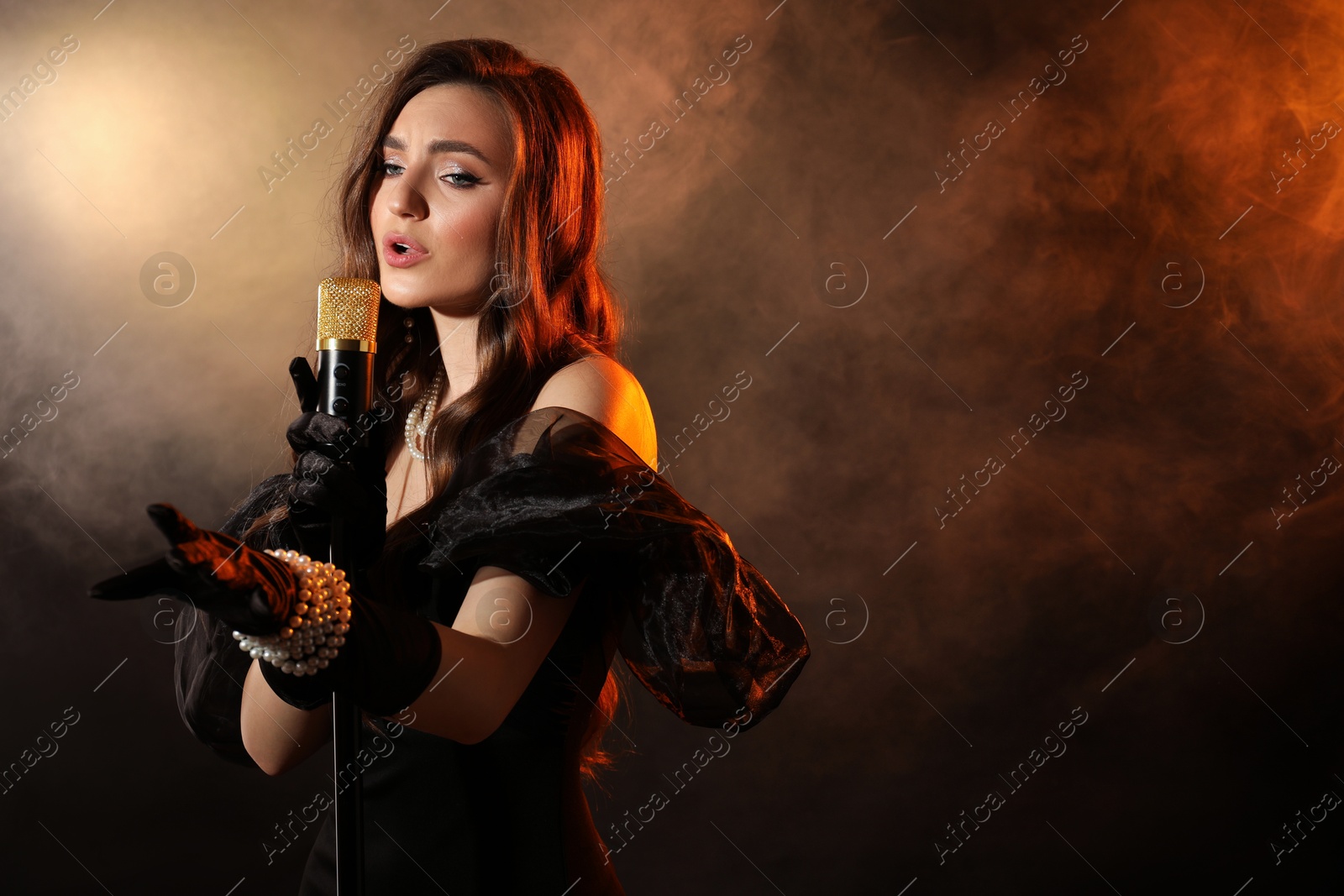 Photo of Beautiful young woman with microphone singing in color lights and smoke, space for text