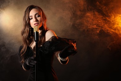 Beautiful young woman with microphone singing in color lights and smoke, space for text