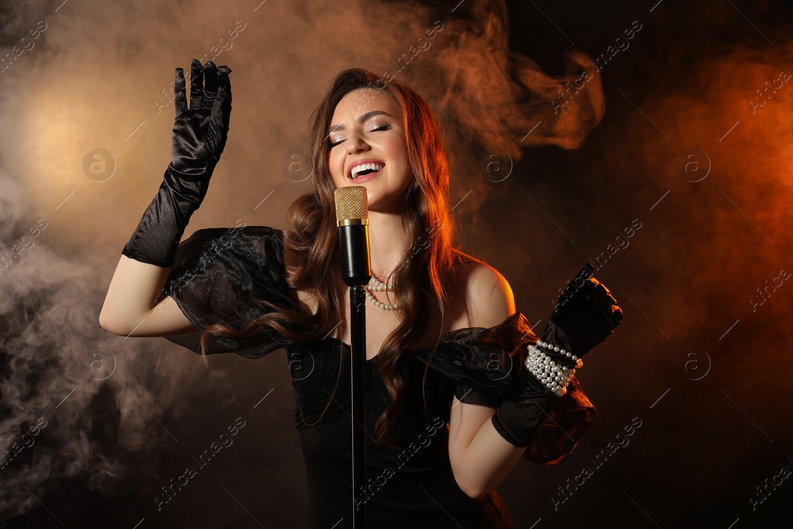 Photo of Beautiful young woman with microphone singing in color lights and smoke