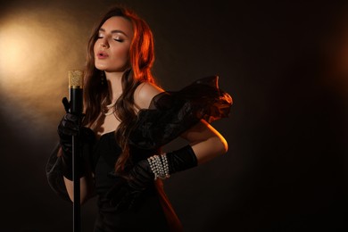 Beautiful young woman with microphone singing on dark background