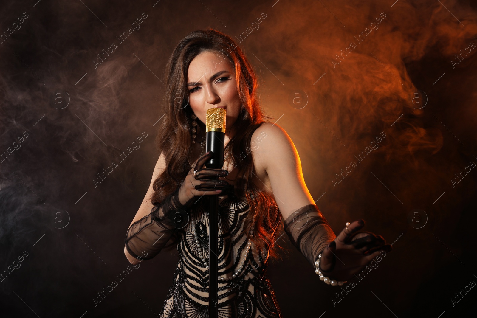 Photo of Beautiful young woman with microphone singing in color lights and smoke