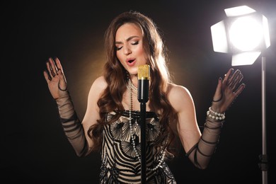 Photo of Beautiful young woman in stylish dress with microphone singing on dark background