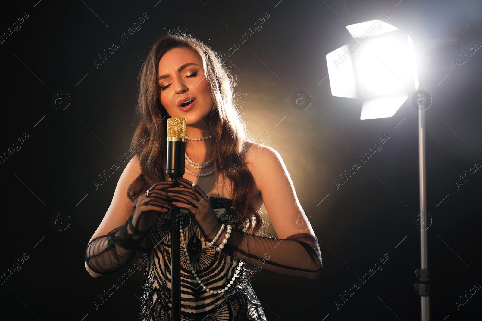 Photo of Beautiful young woman in stylish dress with microphone singing on dark background