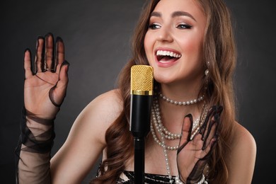 Beautiful young woman with microphone singing on dark background