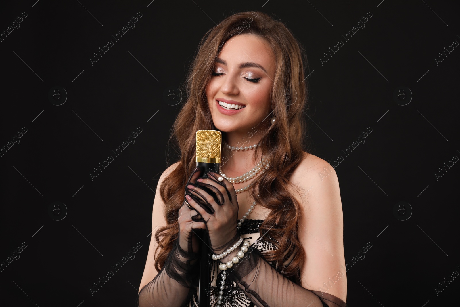 Photo of Beautiful young woman in stylish dress with microphone singing on black background