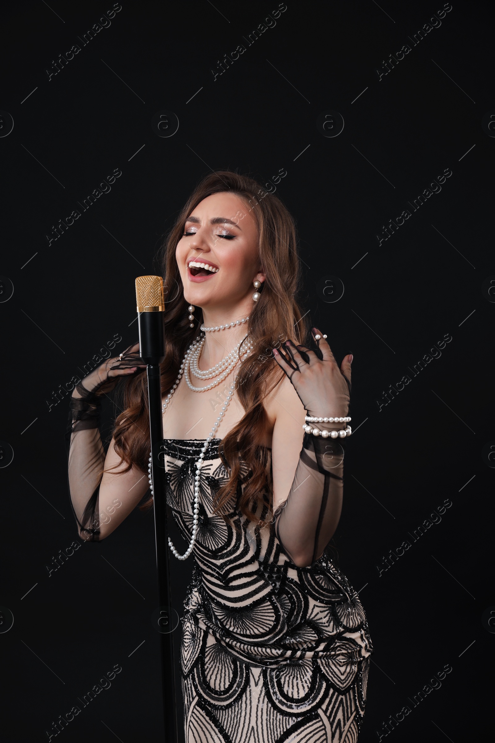 Photo of Beautiful young woman in stylish dress with microphone singing on black background
