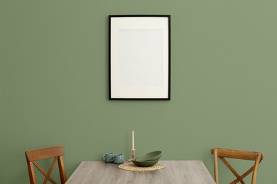 Dining table and chairs near sage green wall indoors. Interior design