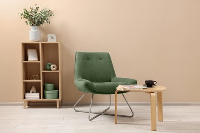 Image of Comfortable armchair, coffee table and shelving unit near beige wall indoors. Interior design