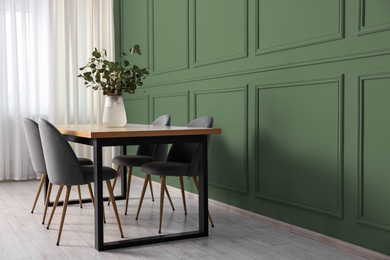 Image of Dining table with chairs near sage green wall in room. Interior design