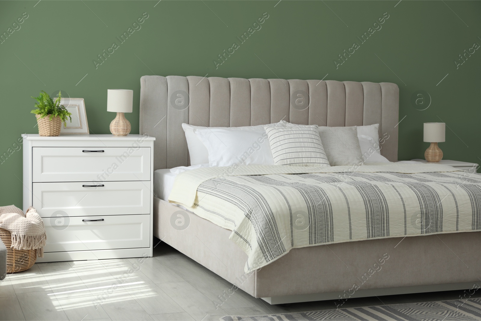 Image of Comfortable bed and chest of drawers near sage green wall in room. Interior design