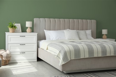 Image of Comfortable bed and chest of drawers near sage green wall in room. Interior design