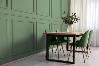 Image of Dining table with chairs near sage green wall indoors. Interior design