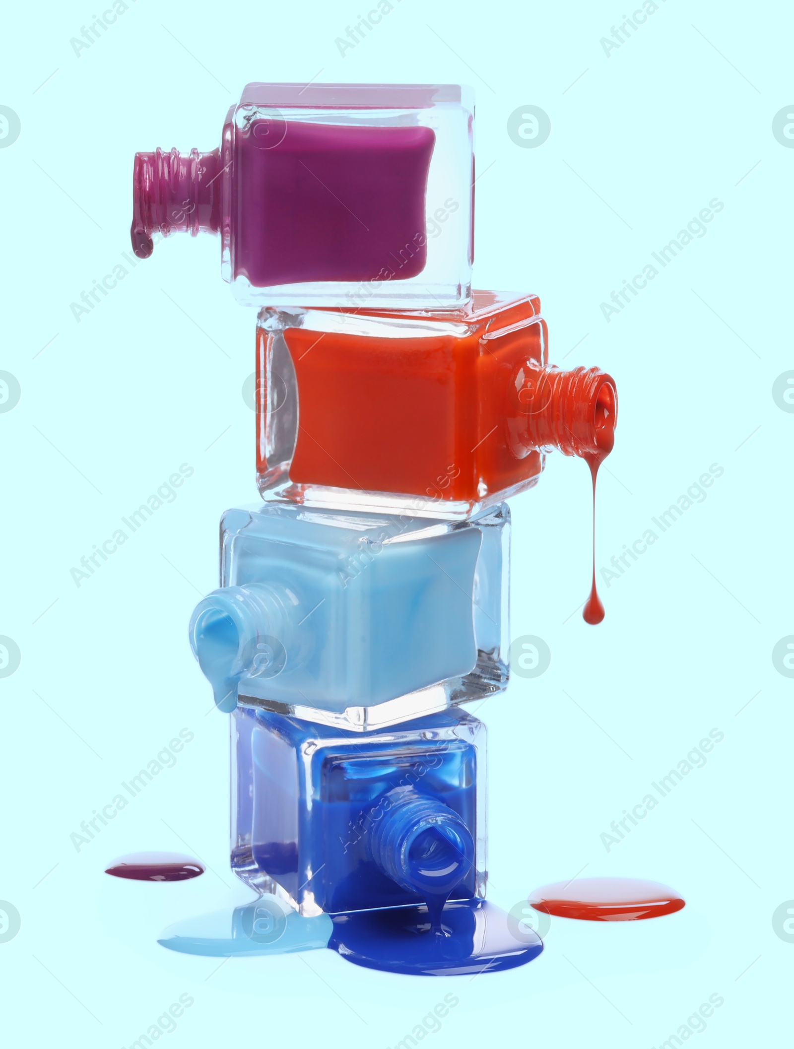 Image of Different nail polishes dripping from open bottles on light blue background