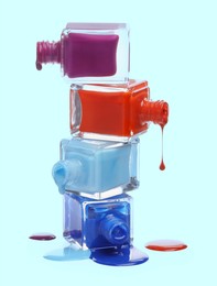 Different nail polishes dripping from open bottles on light blue background