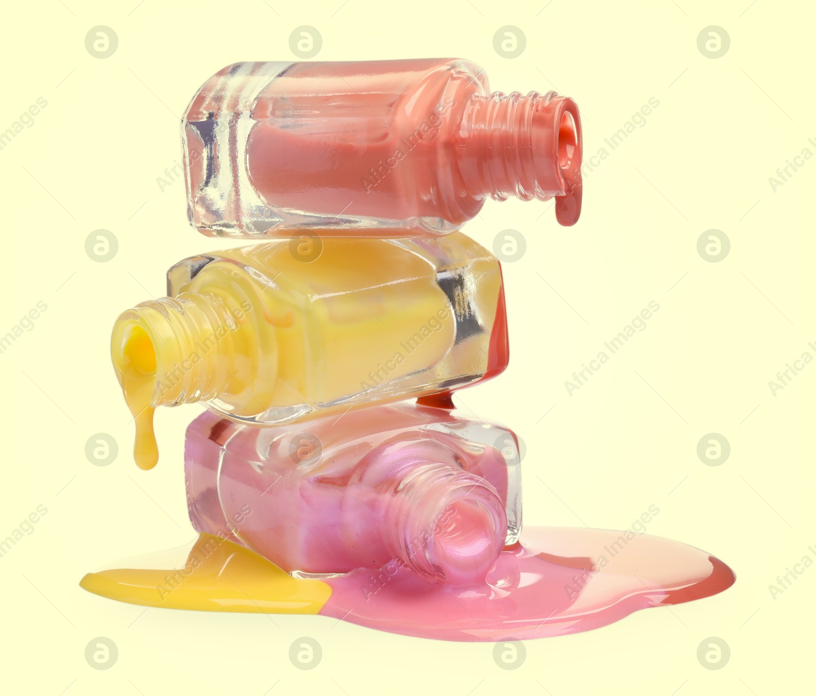 Image of Different nail polishes dripping from open bottles on pale yellow background