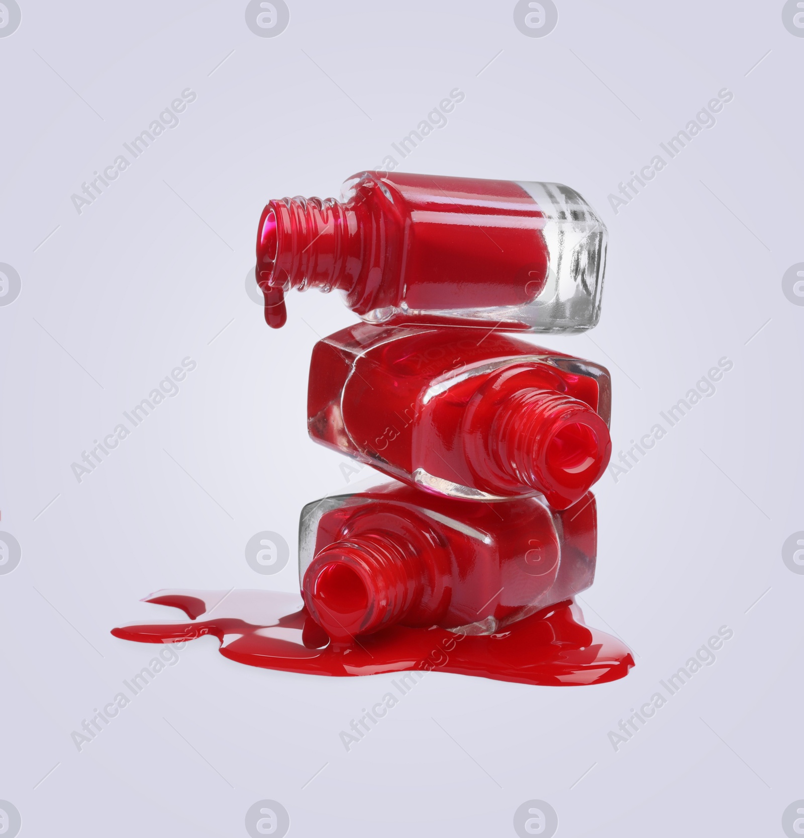 Image of Red nail polish dripping from open bottles on light background