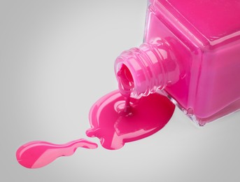 Pink nail polish dripping from bottle on light grey background, closeup