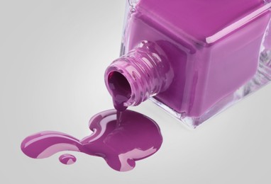 Purple nail polish dripping from bottle on light background, closeup