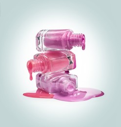 Different nail polishes dripping from open bottles on light background