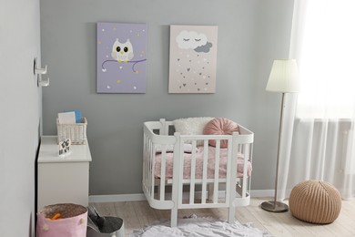 Newborn baby room interior with stylish furniture, comfortable crib and pictures of on wall