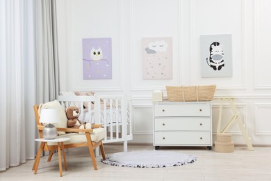 Newborn baby room interior with stylish furniture, comfortable crib and pictures of on wall