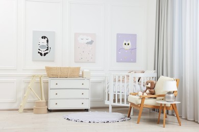 Newborn baby room interior with stylish furniture, comfortable crib and pictures of on wall