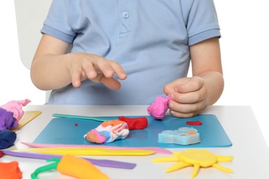 Photo of Little boy sculpting with play dough at table on white background, closeup