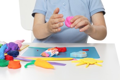 Photo of Little boy sculpting with play dough at table on white background, closeup
