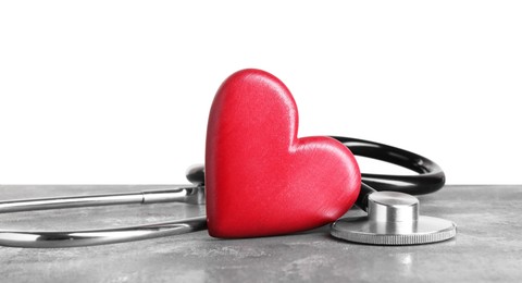 Stethoscope and red heart on grey table against white background