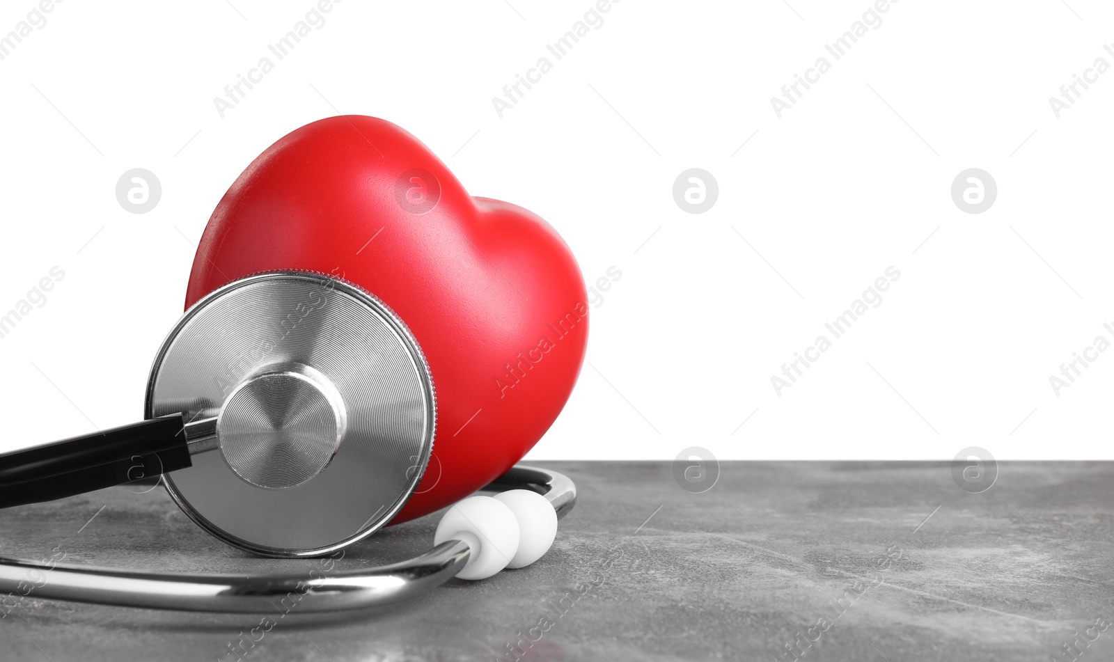 Photo of Stethoscope and red heart on grey table against white background, space for text