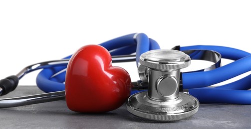 Stethoscope and red heart on grey table against white background