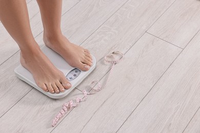 Photo of Woman standing on floor scale and measuring tape at home, closeup. Space for text