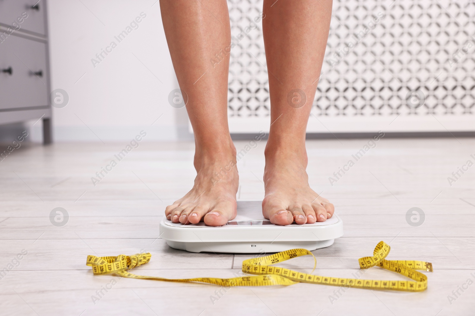 Photo of Woman standing on floor scale and measuring tape at home, closeup. Weight control