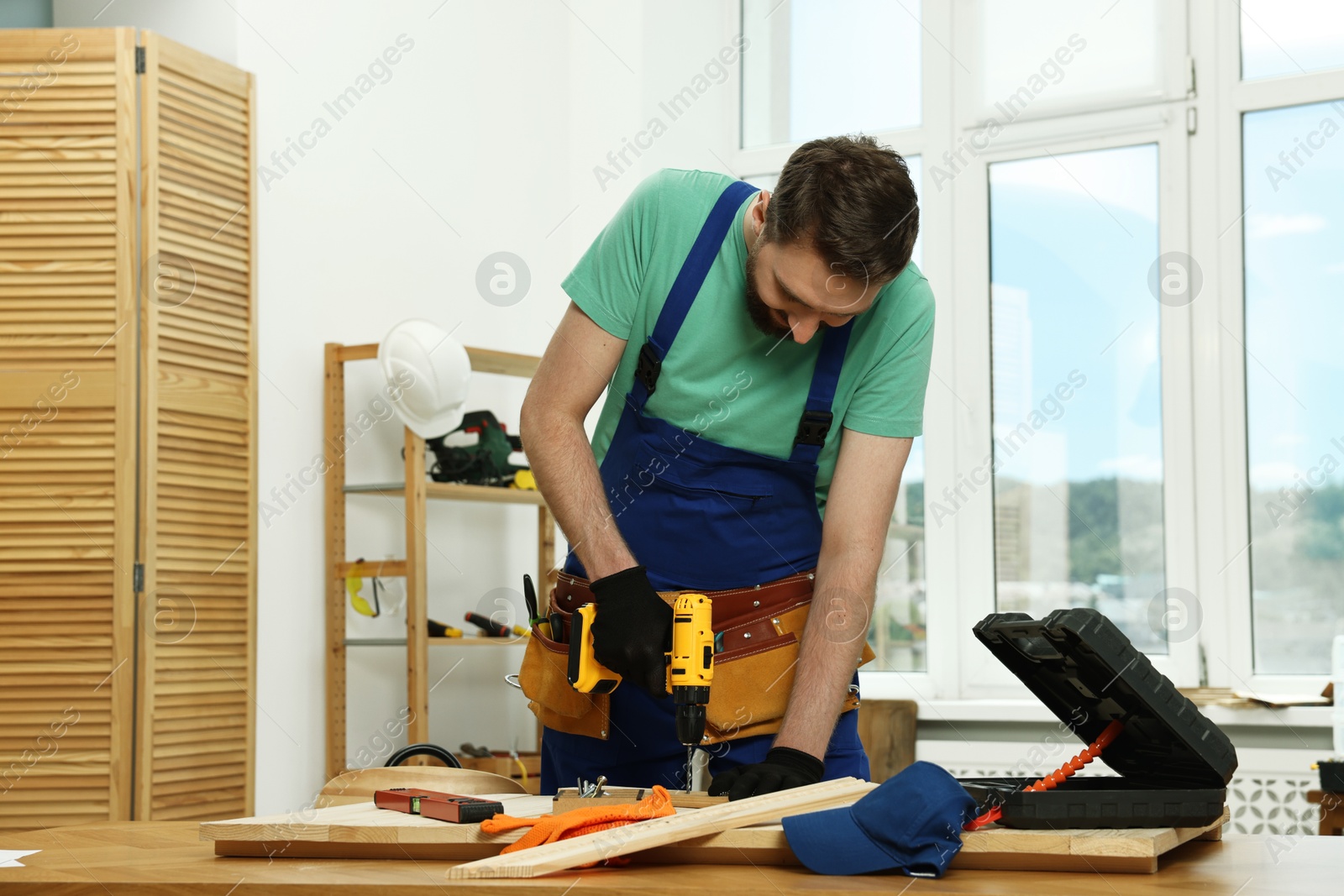 Photo of Craftsman working with drill at wooden table in workshop