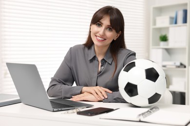 Smiling employee with soccer ball at table in office