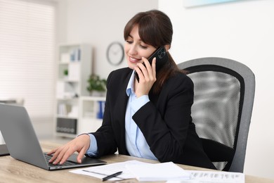 Smiling secretary talking by smartphone at table in office