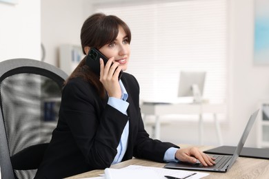 Photo of Smiling secretary talking by smartphone at table in office