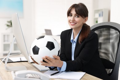 Smiling employee with soccer ball at table in office