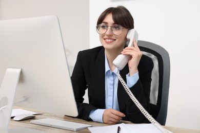 Smiling secretary talking on telephone at table in office