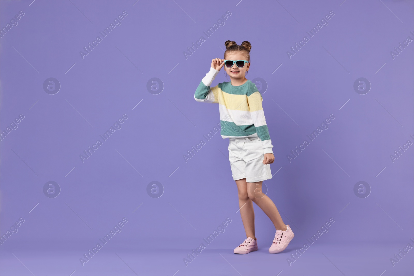 Photo of Cute little girl in sunglasses dancing on violet background, space for text
