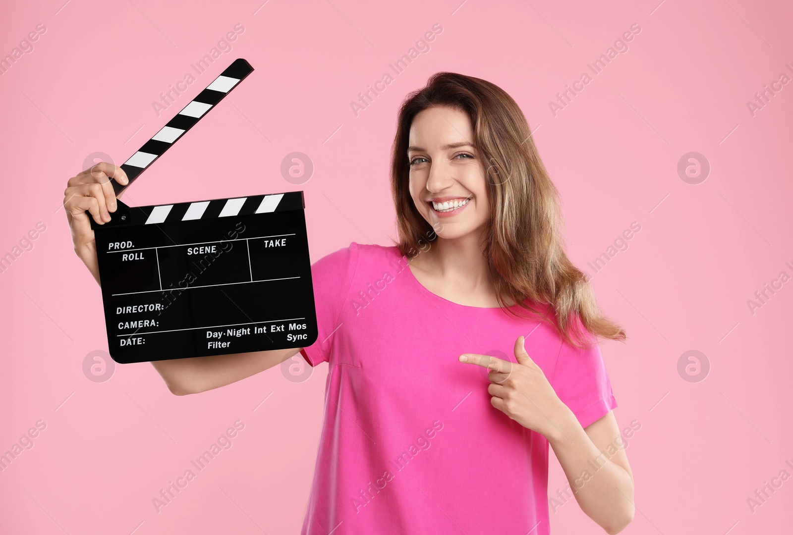 Photo of Making movie. Smiling woman pointing at clapperboard on pink background