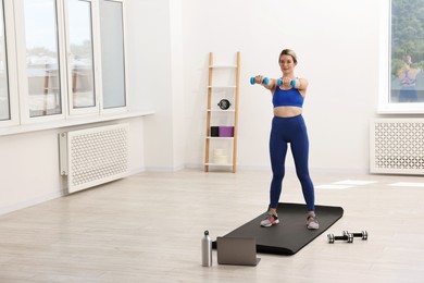 Photo of Online fitness trainer. Woman doing exercise with dumbbells near laptop at home